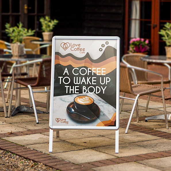 "A-Master signboard displayed outside a café in the UK, showcasing coffee artwork featuring a cup of coffee with latte art and the text 'A COFFEE TO WAKE UP THE BODY.' Perfect for attracting attention and promoting the café's offerings.