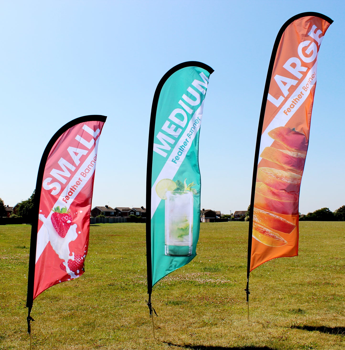 Three feather flying banners lined up outdoors, showcasing small, medium, and large sizes. Each banner features vibrant colors and unique designs, including strawberries on red, lime and mint on green, and orange slices on orange. Ideal for advertising or promotional use, highlighting size options and visual appeal.